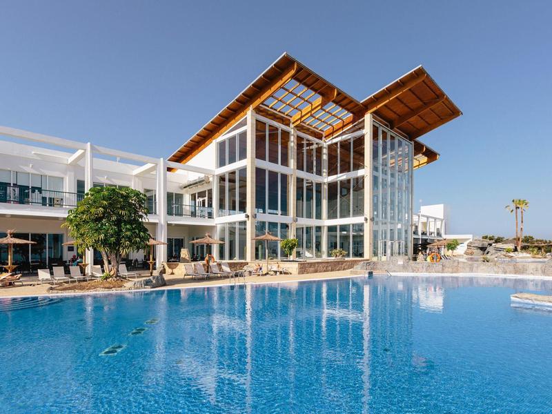 Modern hotel with large glass windows and outdoor pool under a clear sky.