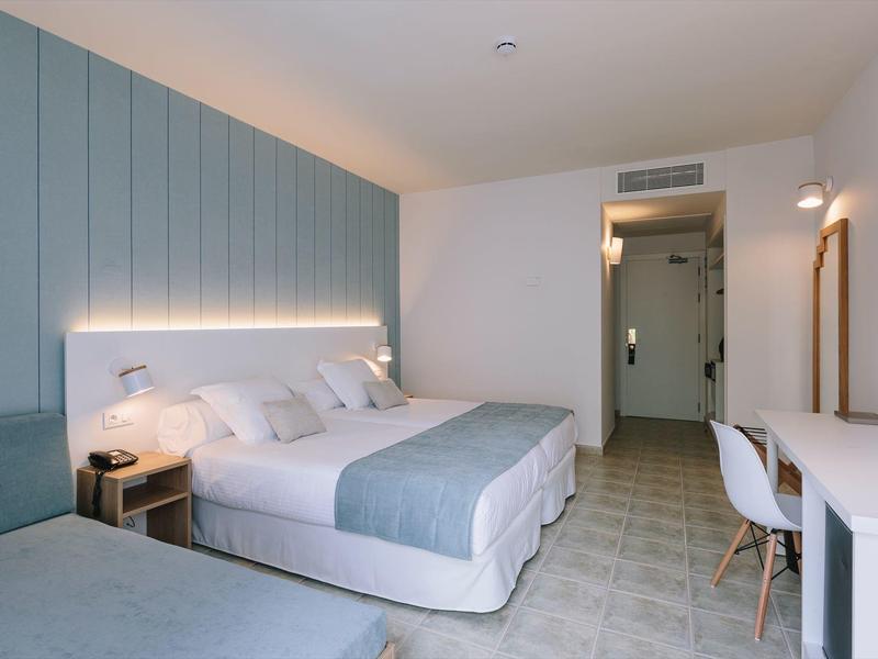 Modern hotel room with a double bed, light blue accents, and a white desk and chair.