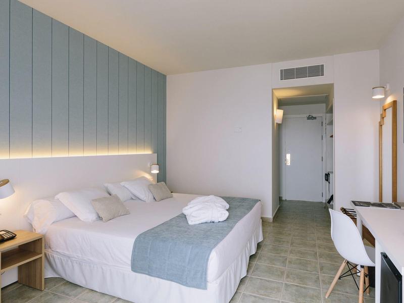 Modern hotel room with a double bed, bedside tables, desk, and neutral decor.