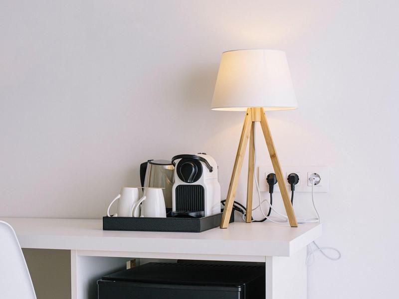 A desk lamp with tripods and a coffee maker with cups on a white desk.