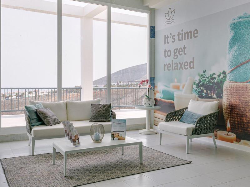 Modern hotel lounge with white chairs, coffee table, and view through large windows.