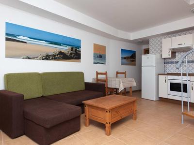 Cozy living room with brown-green sofa, wooden table, and white kitchenette.