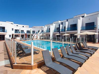 Modern pool area with lounge chairs and white buildings under a clear blue sky.