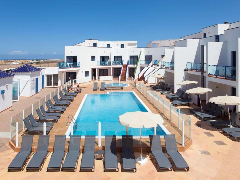 Modern hotel pool with sun loungers and umbrellas under clear blue sky.