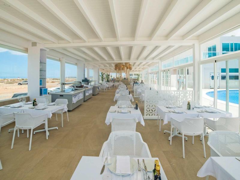 Ampia sala da pranzo luminosa con tavoli e sedie bianchi accanto a una piscina.