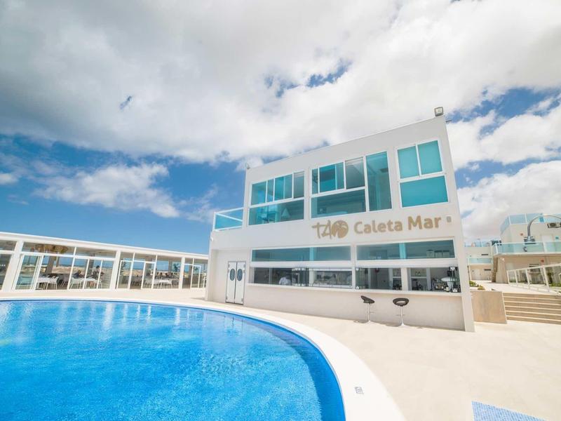 Piscina moderna dell'hotel con acqua azzurra limpida e edificio bianco sotto un cielo nuvoloso.