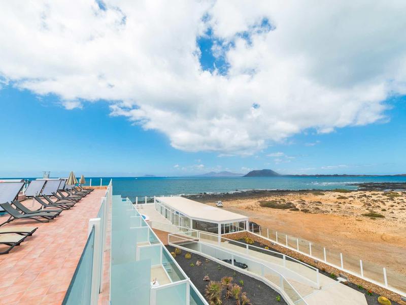 Vista da una terrazza sul tetto con lettini prendisole che si affaccia sul mare e sul paesaggio costiero.