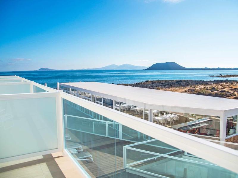 Balcone moderno con ringhiera in vetro e vista sul mare sotto un cielo limpido.