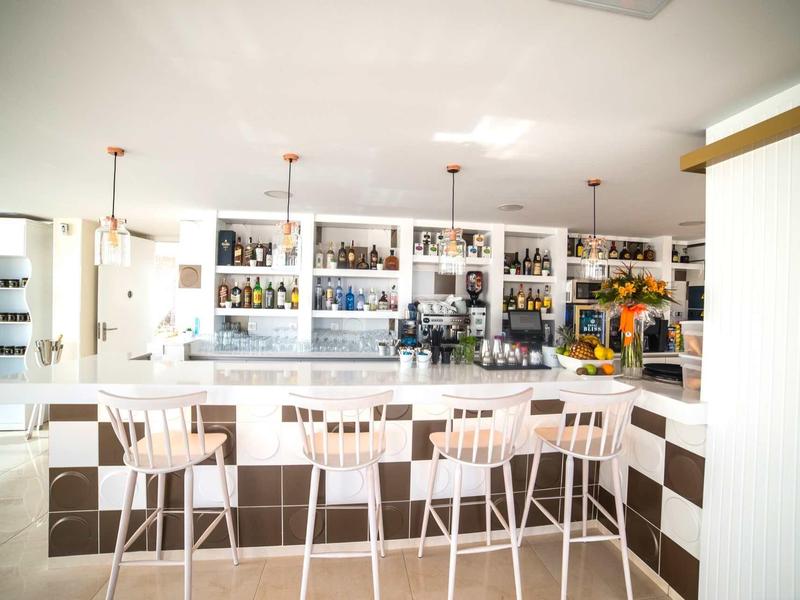 Bar moderno con sgabelli bianchi e scaffali ben forniti in un ambiente luminoso.