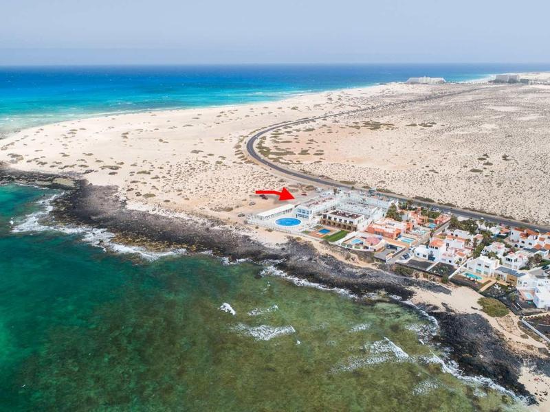 Spiaggia rocciosa e sabbiosa con acqua limpida e diversi edifici lungo la costa.