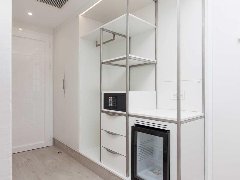 Corridoio dell'hotel luminoso con scaffali incorporati, una piccola cassaforte e un mini frigorifero.