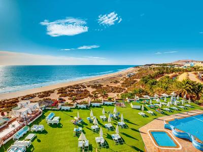 Hotel z leżakami, basenem i widokiem na plażę pod niebieskim niebem nad morzem.