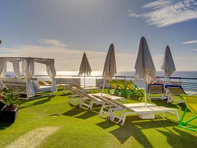 Terrazza solare con lettini, ombrelloni e vista sul mare sotto un cielo limpido.