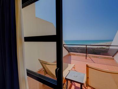 Vista dal balcone della camera sulla terrazza con sedie e mare all'orizzonte sotto un cielo limpido.
