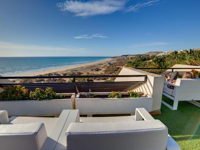 Vista sulla costa da una terrazza con sedie bianche e fioriere.