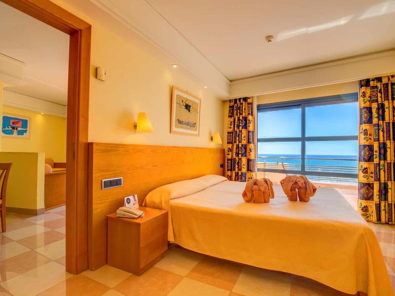 Camera d'hotel con letto matrimoniale, mobili in legno e vista mare dalla finestra grande.
