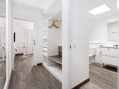 Camera d'hotel moderna con pavimento in legno, armadio aperto, specchio e bagno luminoso.