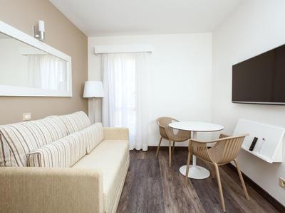 Soggiorno moderno con divano beige, tavolo rotondo e TV a muro.