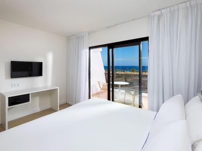 Camera d'albergo luminosa con letto bianco e vista mare dalla terrazza.