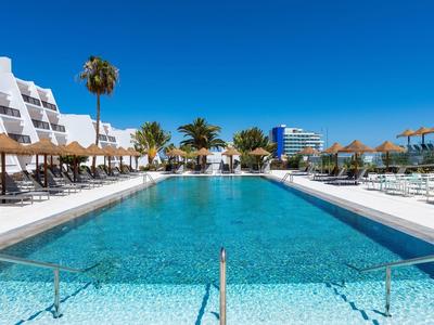 Großer Hotelpool mit Liegestühlen, Palmen und klarem blauem Himmel.