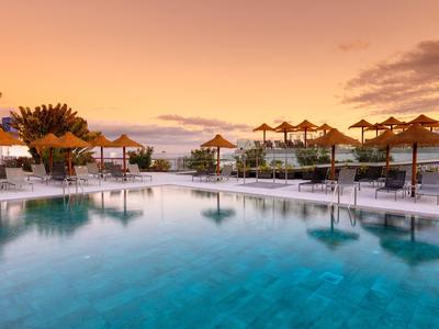 Duży basen z parasolami i leżakami o zachodzie słońca w ośrodku.