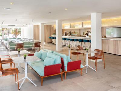 Salotto d'hotel moderno con poltrone colorate e bar illuminato, atmosfera accogliente e spaziosa.