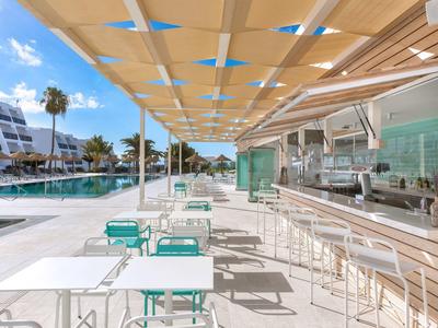 Terrazza ombreggiata con tavoli, sedie e bar vicino a piscina in hotel moderno.
