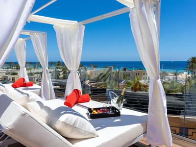 Luxurious terrace with white loungers, red pillows, and sea view under sunny skies.