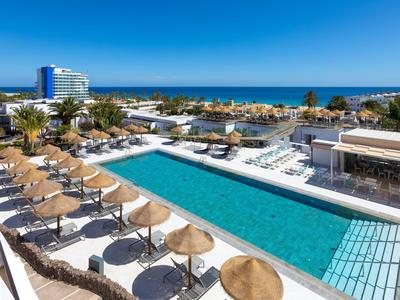 Modern hotel pool with loungers and parasols by the sea.
