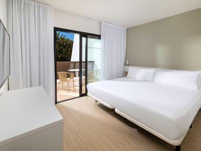 Bright hotel room with double bed, balcony, and modern furnishings.
