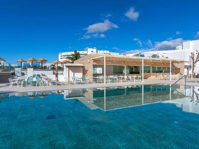 Modern hotel pool with clear water and cozy lounge under a blue sky.