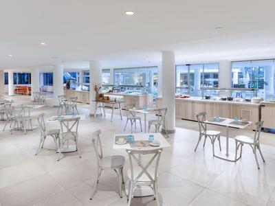 Bright, modern dining area with white tables and metal chairs in a hotel.