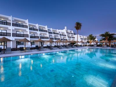 Modern hotel complex with illuminated pool and sun loungers at dusk.