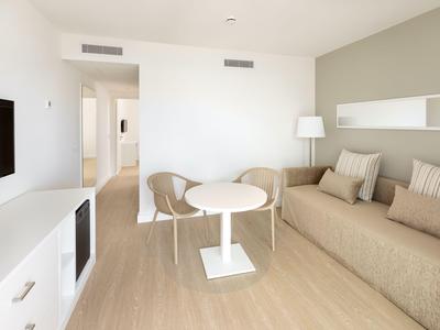 Bright hotel room with cozy sofa, small round table, and chairs, minimally furnished.