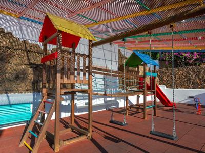 Children's playground with wooden towers, slides, and swings on paved ground.