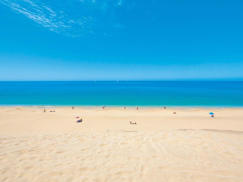 Spiaggia di sabbia fine con cielo azzurro e mare calmo.