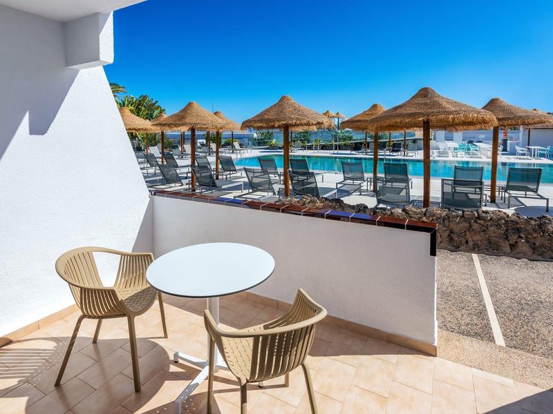 Terrazza con tavolo e sedie, vista su piscina e ombrelloni vicino al mare.