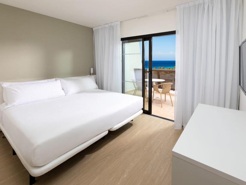 Camera d'hotel moderna con letto matrimoniale, balcone e vista mare.