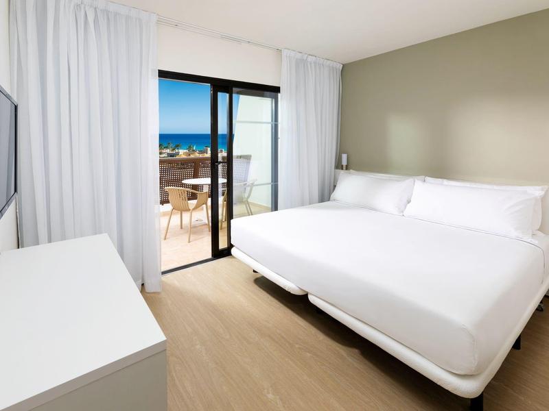 Camera moderna con letto matrimoniale, balcone vista mare e arredamento semplice.