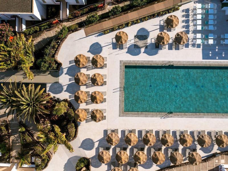 Piscina azzurra circondata da lettini e ombre di alberi.