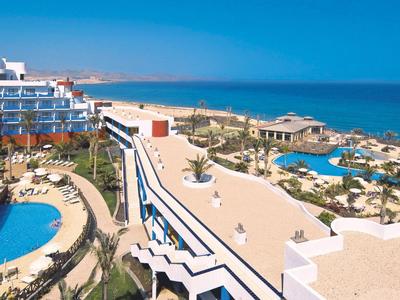 Hotelanlage mit Swimmingpools, Liegestühlen und Blick auf das Meer bei klarem Himmel.