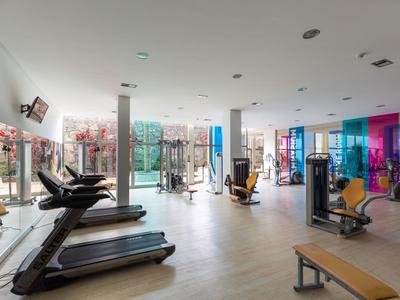 Großer, heller Fitnessraum mit Laufbändern, Kraftgeräten und bunten Fenstern.