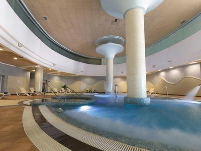 Moderner Indoor-Schwimmbadbereich mit Whirlpool, Säulen, Holzdecke und entspannenden Sitzplätzen.
