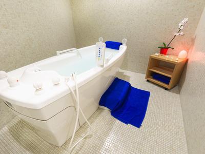 Moderne weiße Badewanne mit blauer Matte und Schale im hellen, kleinen Badezimmer.
