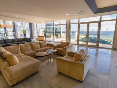 Großes Wohnzimmer mit beige Sofa, Glasfenstern und Blick auf das Meer bei Sonnenschein.
