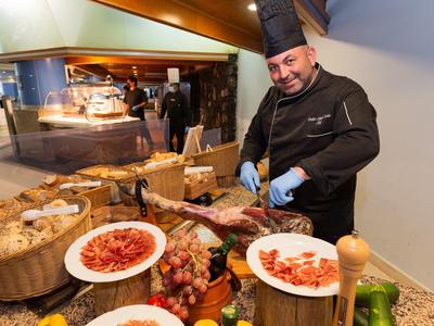 Ein Koch mit Kochmütze schneidet an einem Buffet mit verschiedenen Lebensmitteln.