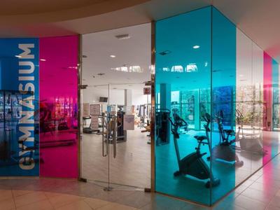 Eingang zu einem modernen Fitnessstudio mit bunten Glaswänden in Blau und Pink.