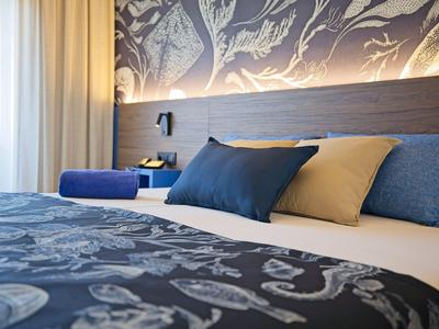 Modernes Hotelzimmer mit gemustertem Bettüberwurf und mehreren Kissen auf dem Bett.