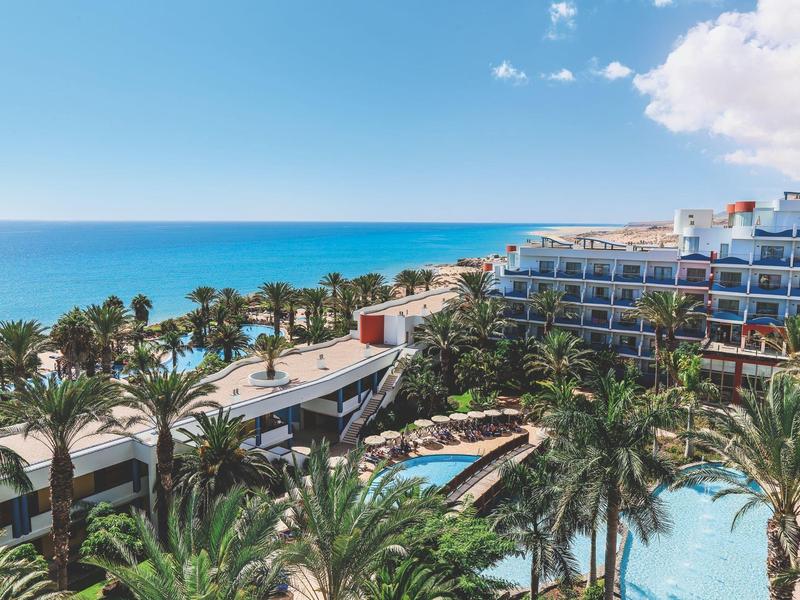 Hotel sulla spiaggia con piscine e palme vicino al mare blu sotto un cielo limpido