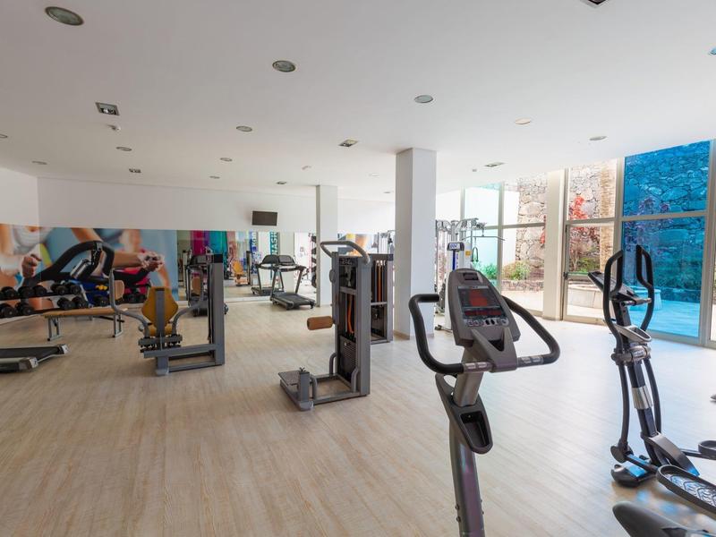 Palestra moderna con varie attrezzature per esercizi e grandi finestre con vista su una parete esterna.